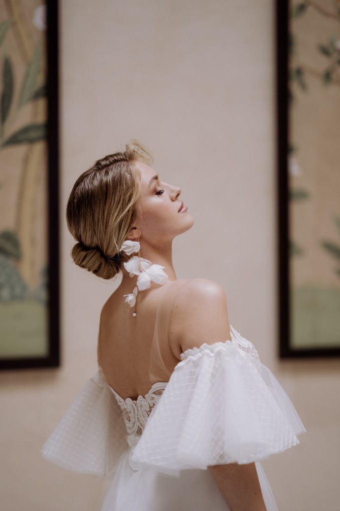 Brautkleid ‚Jackie‘ aus transparentem Tüll mit femininer, figurbetonter Silhouette, drapierten Fächerärmeln und kurzem Unterrock. Modernes, leichtes Design mit verträumtem, trendigem Look für stilbewusste Bräute.