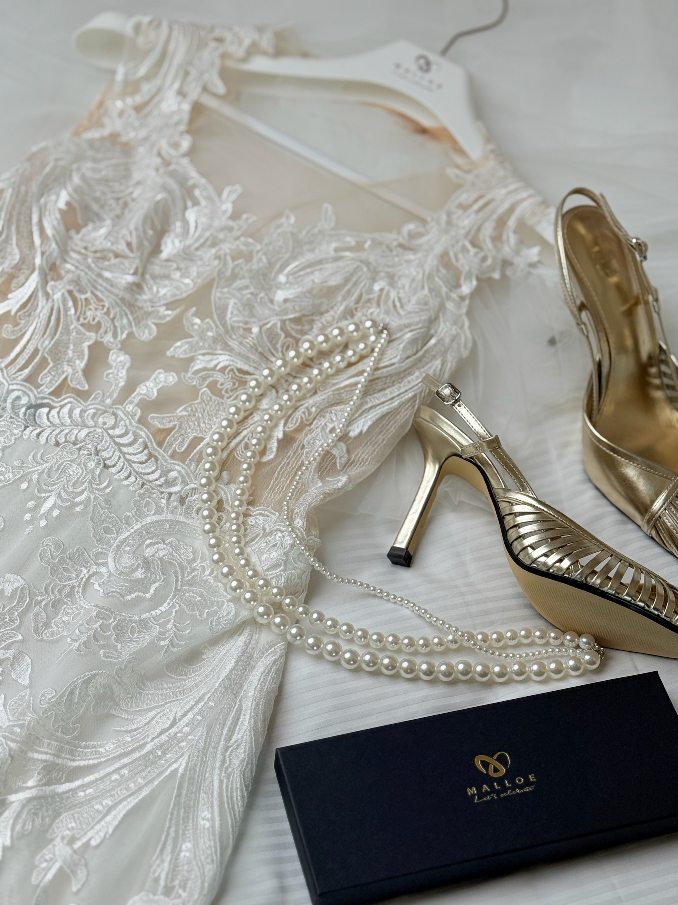Die Details des Tages Brautschuhe, Perlenkette und goldene Brautschuhe von MALLOE neben einem spitzen Standesamtkleid