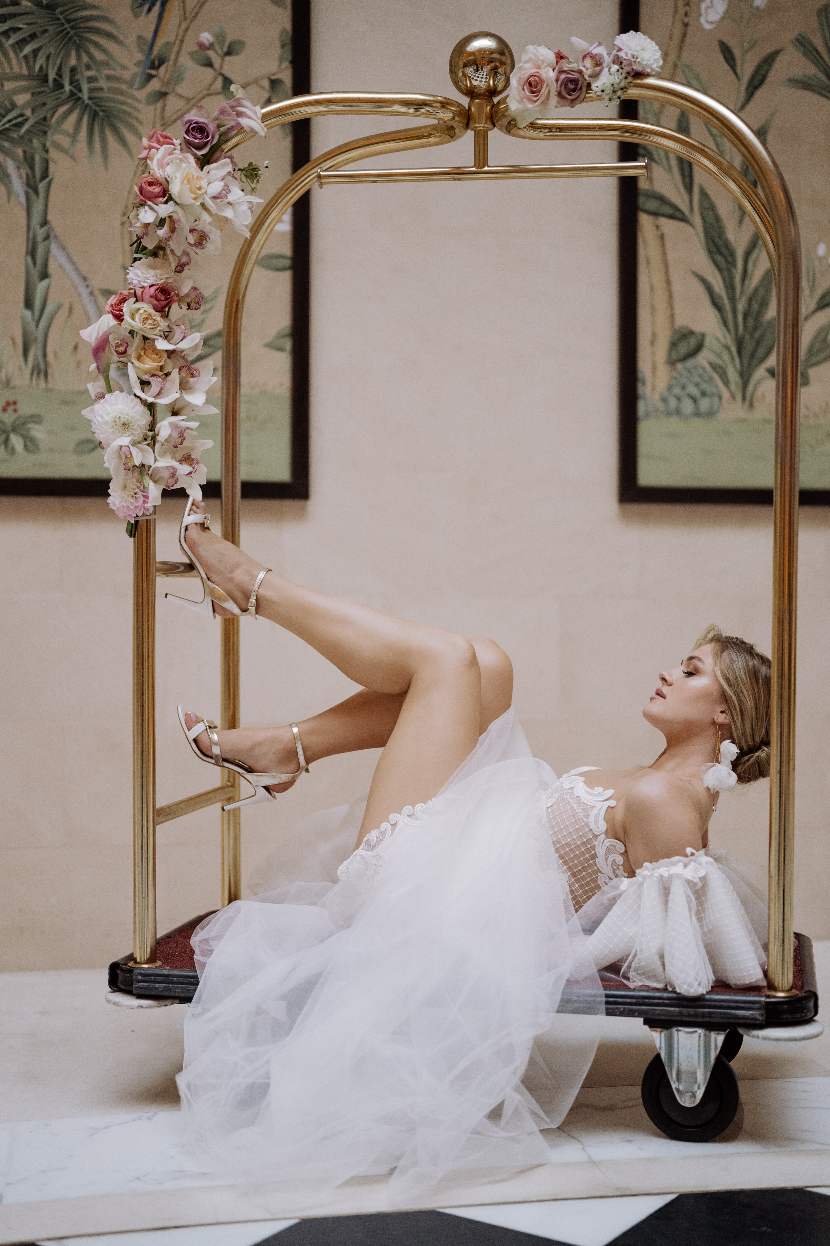 Wie finde ich mein perfektes Brautkleid? 10 goldene Regeln, die alles perfekt machen. 2 Braut in einem Tüll-Brautkleid von MALLOE mit Sandalen auf einem goldenen Hotel-Gepäckwagen