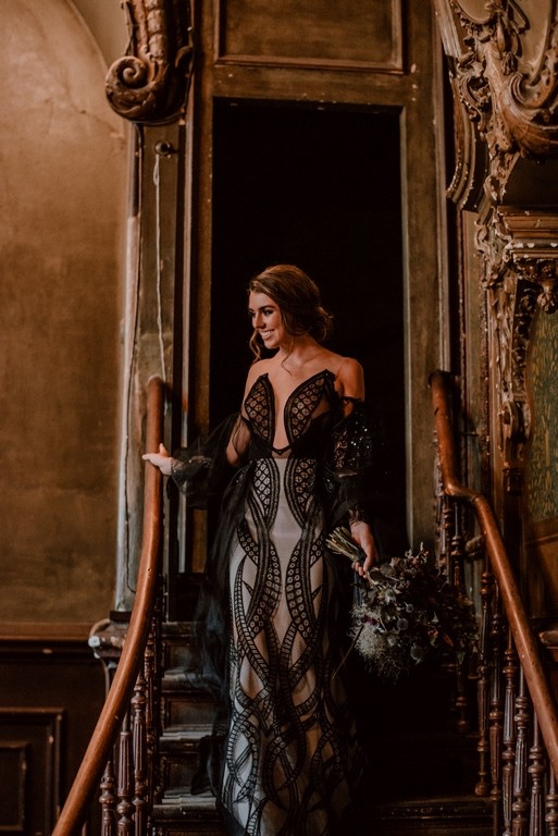 Braut in einem schwarzen Spitzenbrautkleid mit geometrischem Muster auf einer historischen Treppe