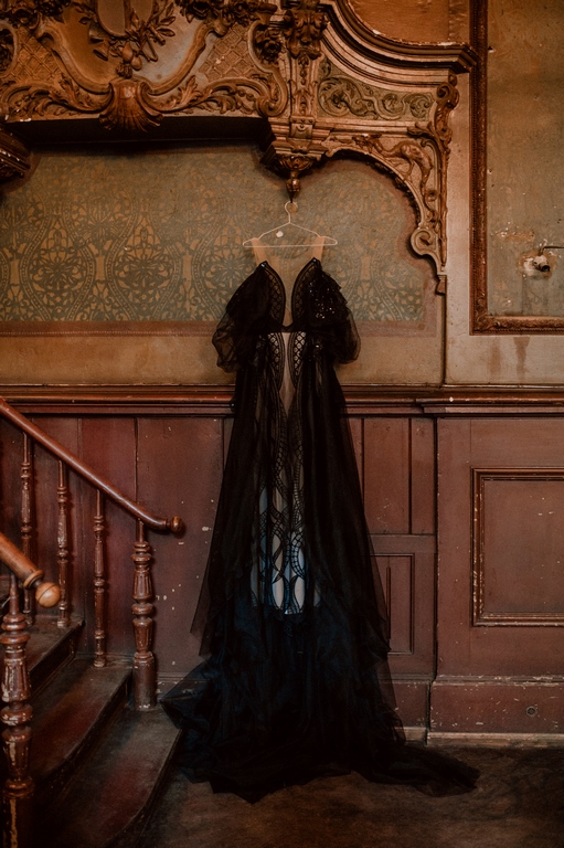 Schwarzes Brautkleid aus Spitze mit transparenten Ärmeln und fließendem Tüllrock, elegant präsentiert auf einem Kleiderbügel