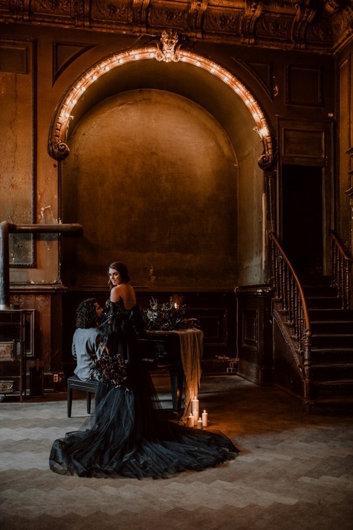 Braut im schwarzen Brautkleid mit langer Schleppe an einem Klavier in einem historischen Ballsaal