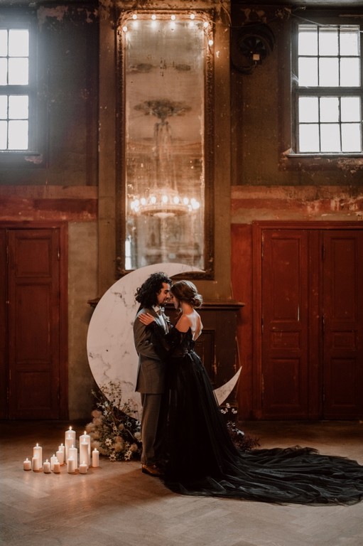 Brautpaar in schwarzem Brautkleid und elegantem Anzug vor einer großen Monddekoration bei einer Vintage-Hochzeit