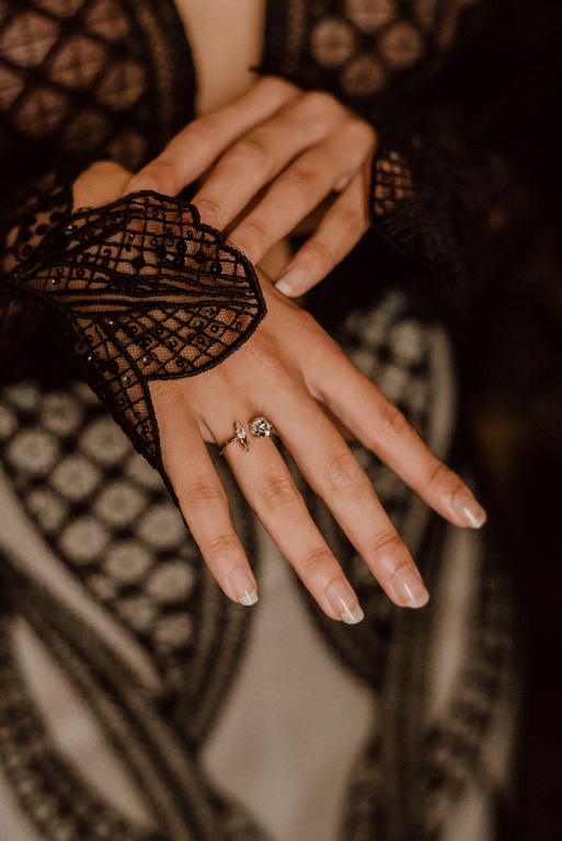 Detailaufnahme eines Rings an der Hand einer Braut mit schwarzem Spitzenärmel